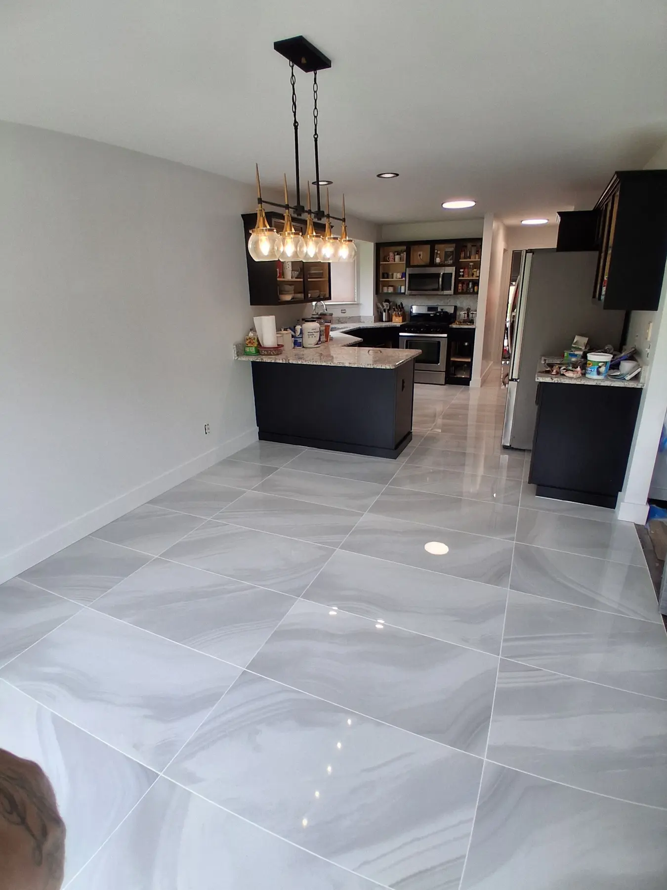 Dining area and kitchen with a polished grey porcelain floor, black cabinets and a five-globe pendant