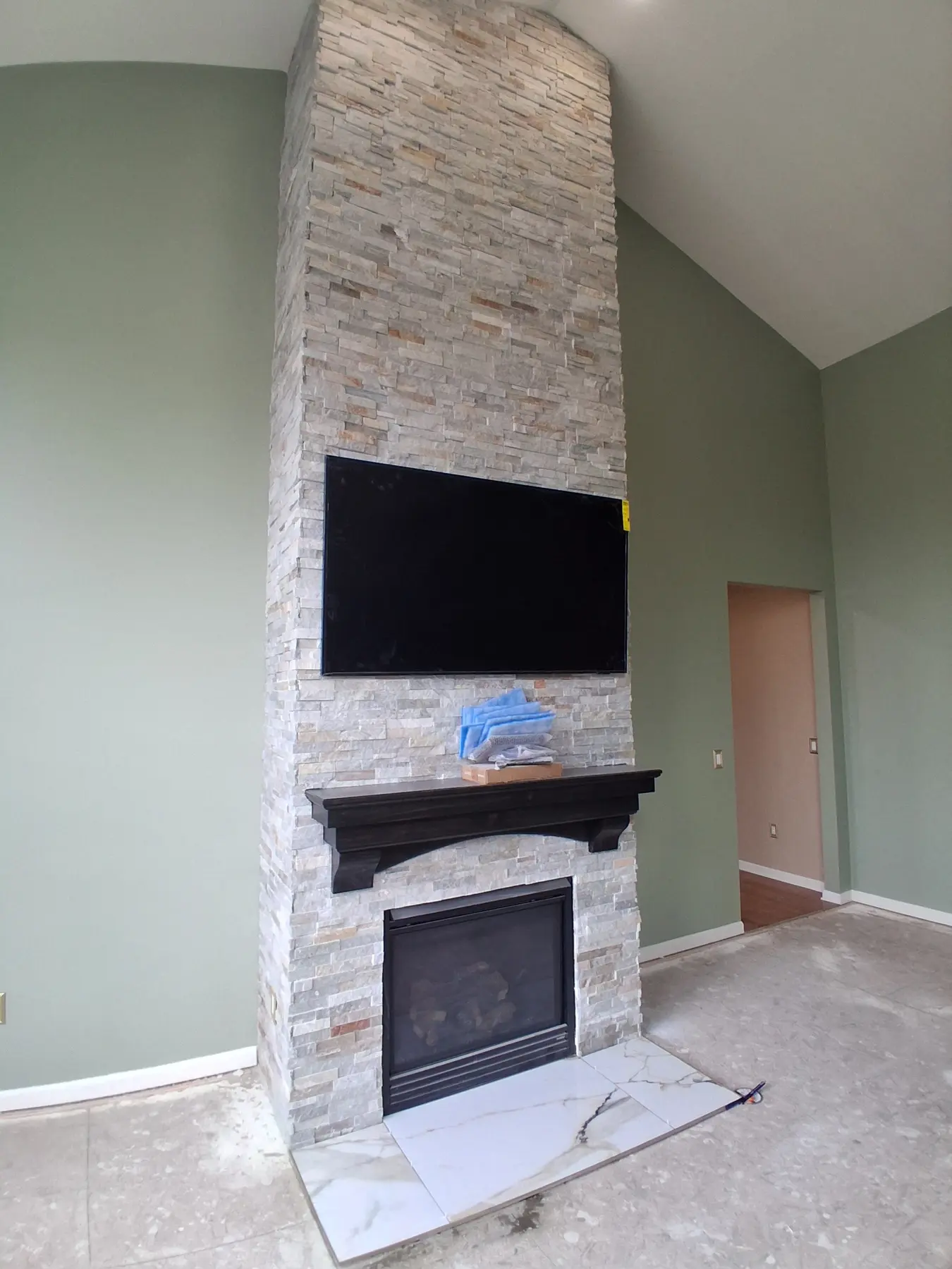 Floor-to-ceiling stacked stone fireplace with a dark wood mantel and a wall-mounted television